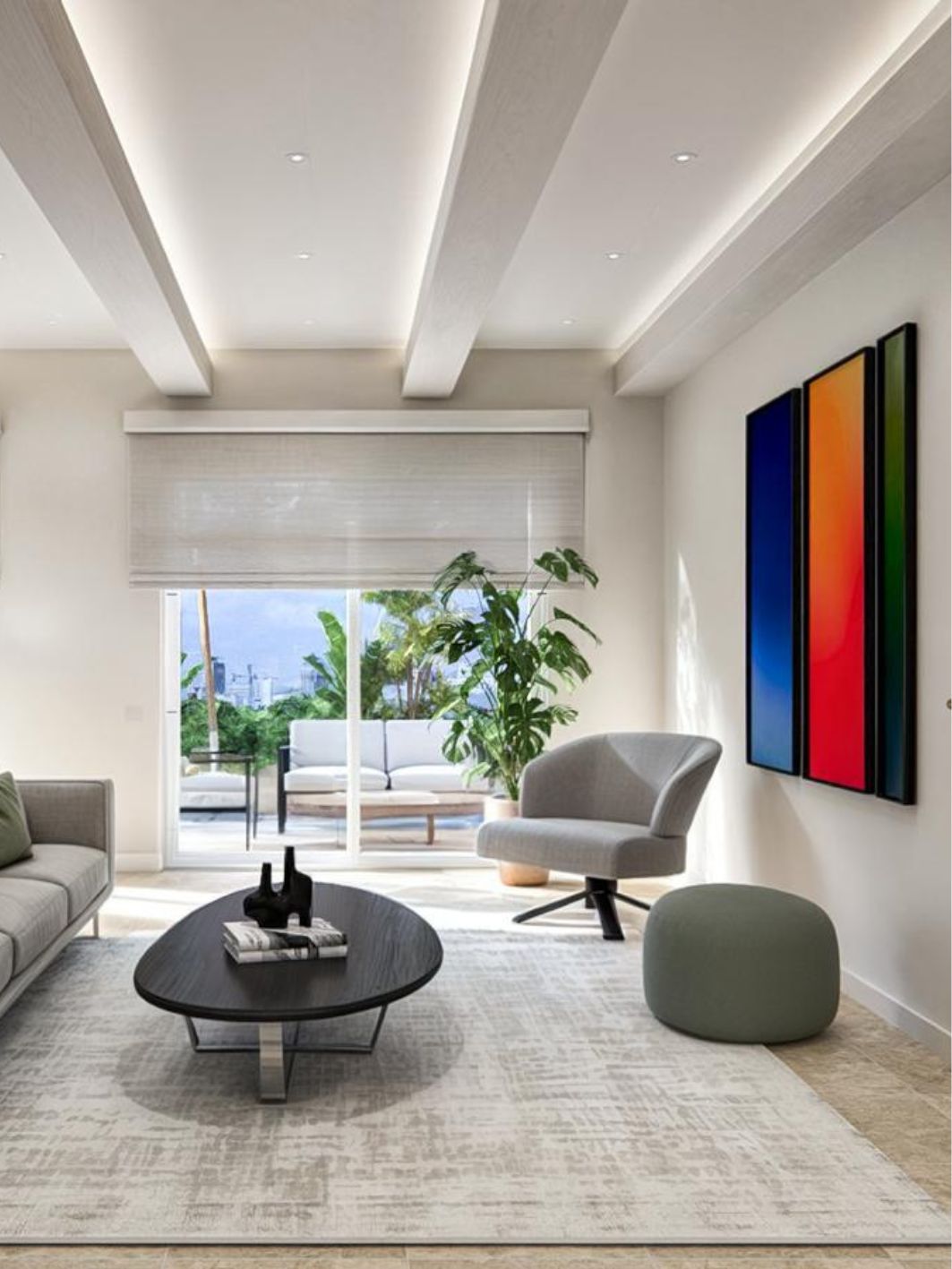 Living room with a slatted white beam ceiling and cove lighting, a triptych of colour-field canvases, grey swivel armchair, sage pouf, black oval coffee table and sliding doors onto a planted terrace