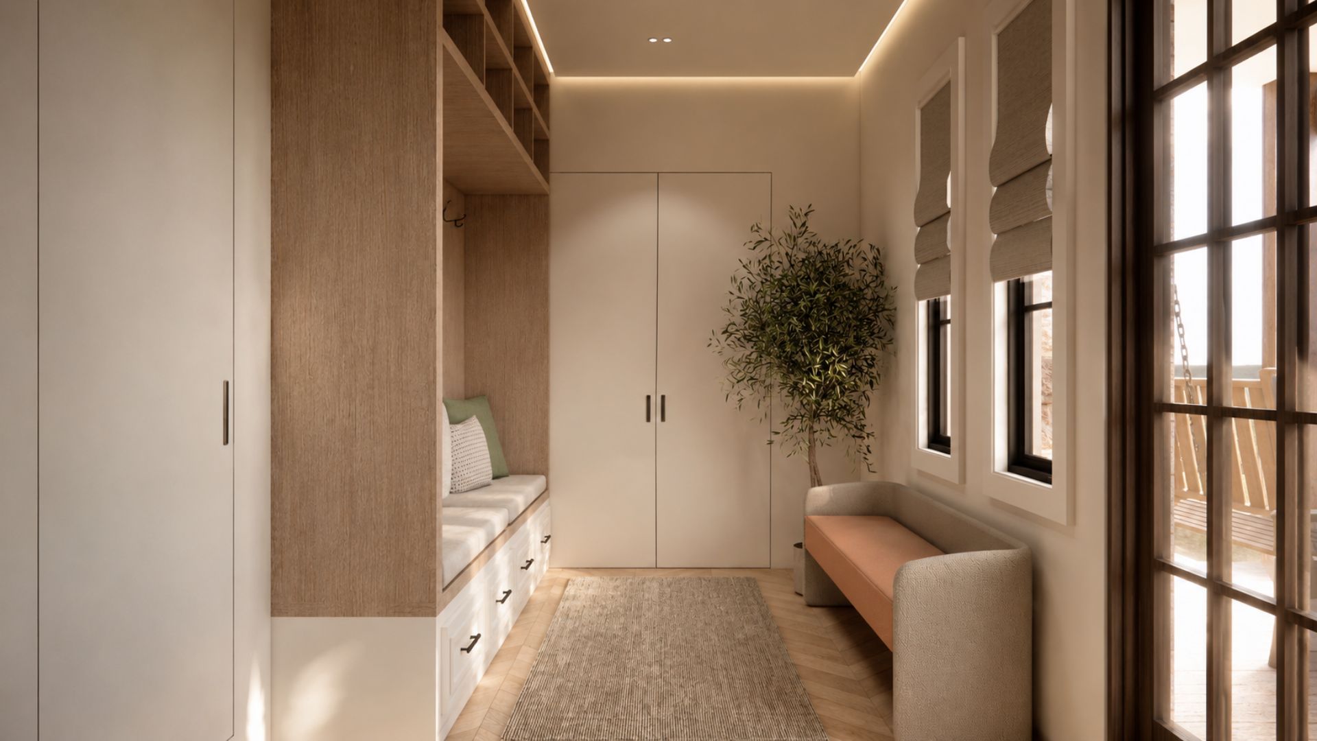 Long view down the entry vestibule with full-height cream joinery, an oak bench nook with cove lighting, an olive tree and black-framed windows with linen roman blinds over a woven runner