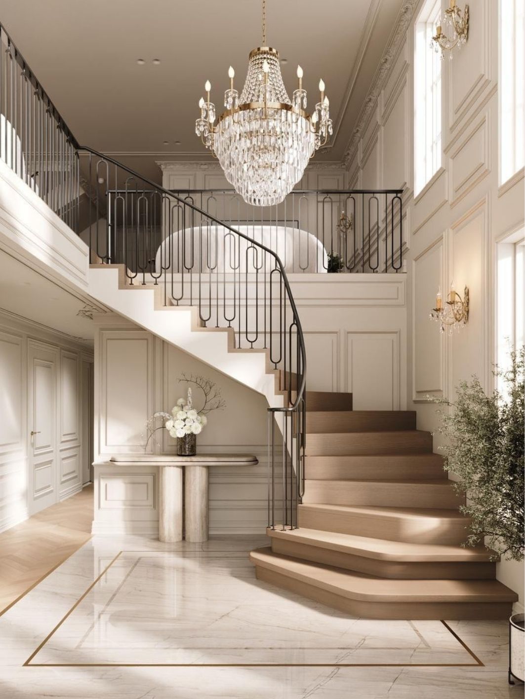 Wide view of the entrance hall with the curving oak staircase and ironwork balustrade, crystal basket chandelier, brass wall sconces, a stone console with white blooms and a brass-inlaid marble floor