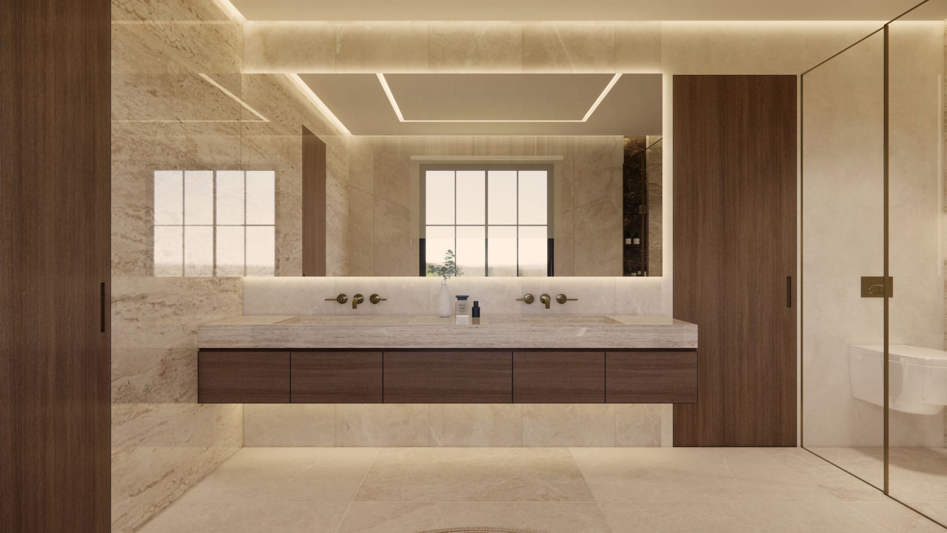 Bathroom vanity in cream travertine with twin integrated basins, bronze wall-mounted taps, walnut drawer fronts, a full-width backlit mirror and a glass-screened WC beyond
