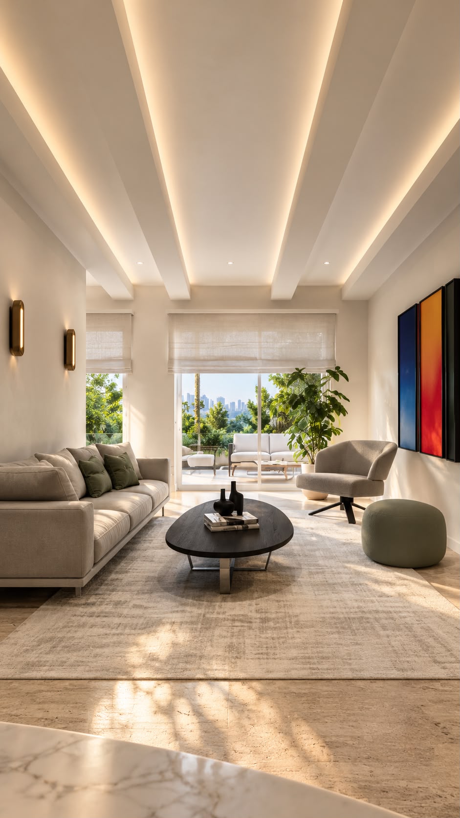 Centered living room view with a coffered ceiling and linear recessed lighting, a long light-grey fabric sofa, oval black coffee table, grey armchair with a sage-green circular ottoman, two long gold wall sconces, three colour-field canvases on the right wall and a view through the balcony door to trees, outdoor seating and the skyline beyond