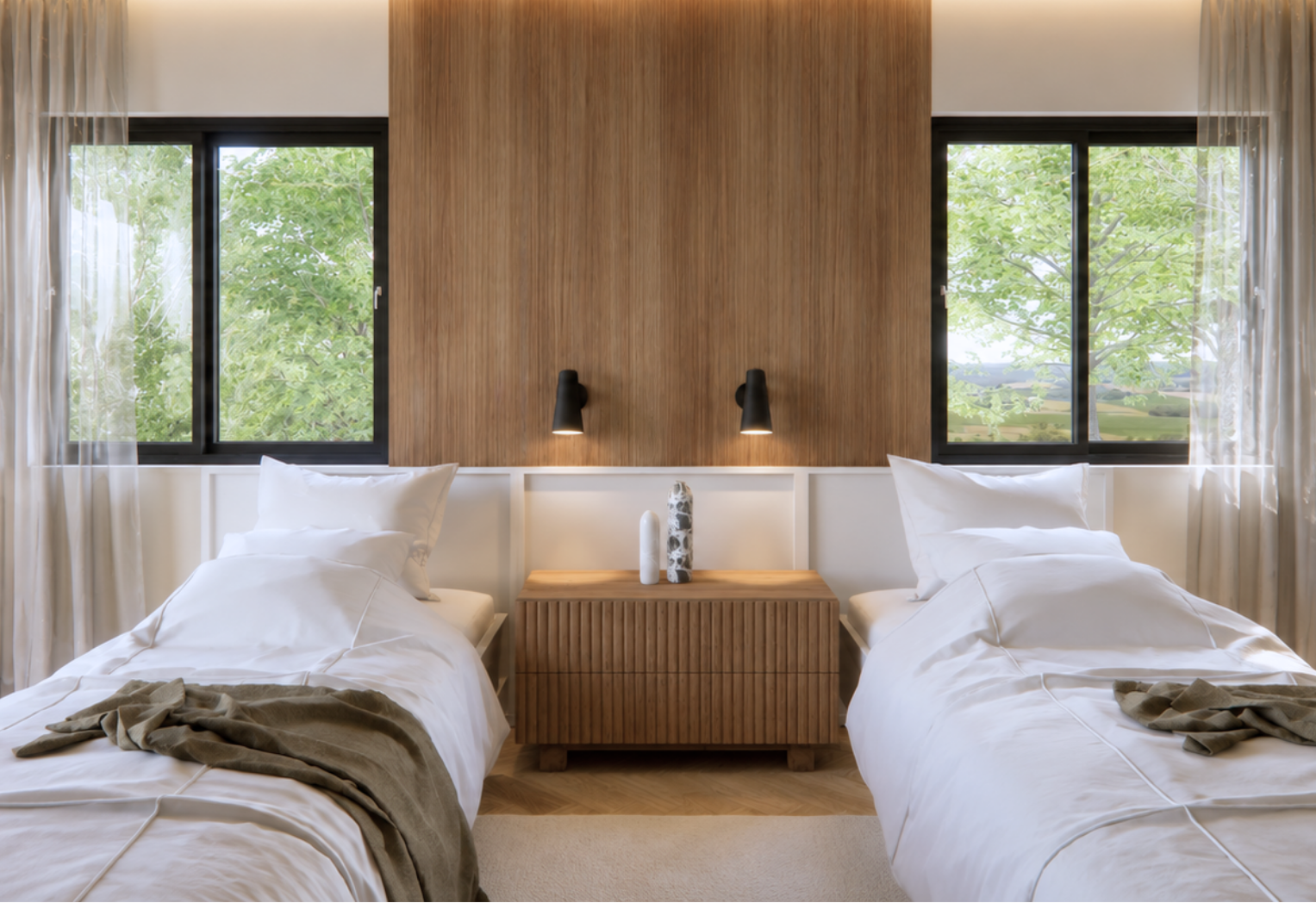 Symmetrical bedroom with two twin beds in white linens and olive throws, a fluted wood nightstand between them, a floor-to-ceiling wood panel accent wall flanked by black-framed windows onto trees and black reading sconces on a herringbone oak floor