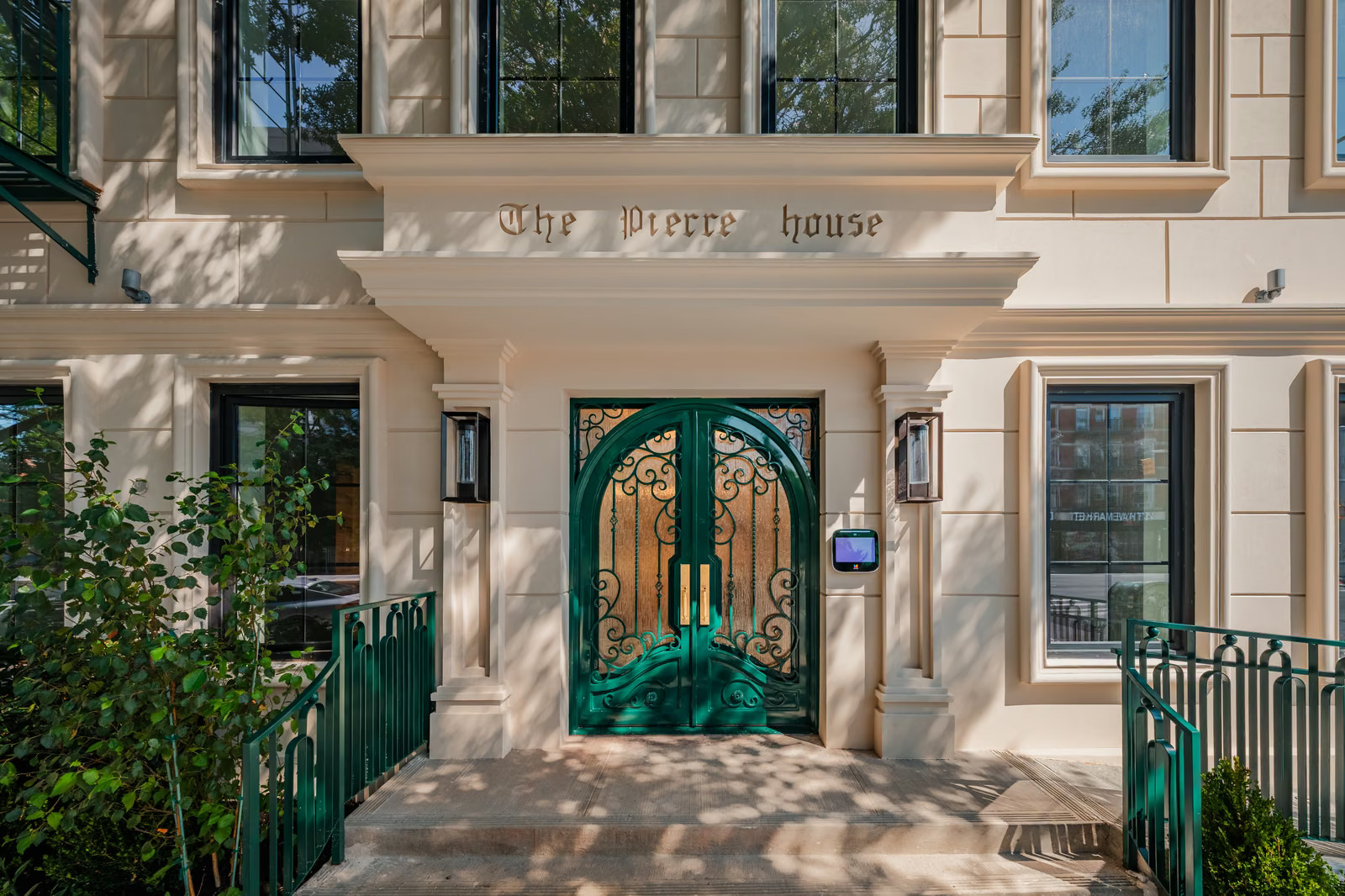 Main entrance with an arched green door in scrolled ironwork over timber, gilded 'The Pierre House' lettering on the cast-stone lintel, bronze lanterns and green railings
