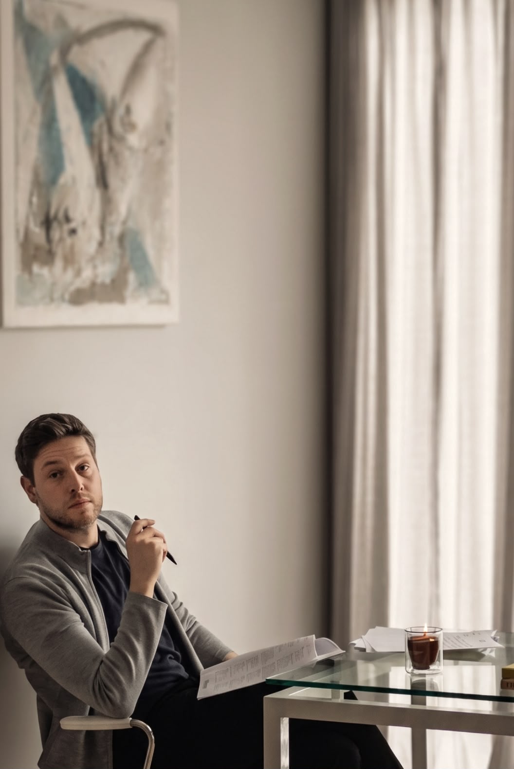 Pierre Miller seated at a glass desk with drawings, an abstract canvas on the wall behind him
