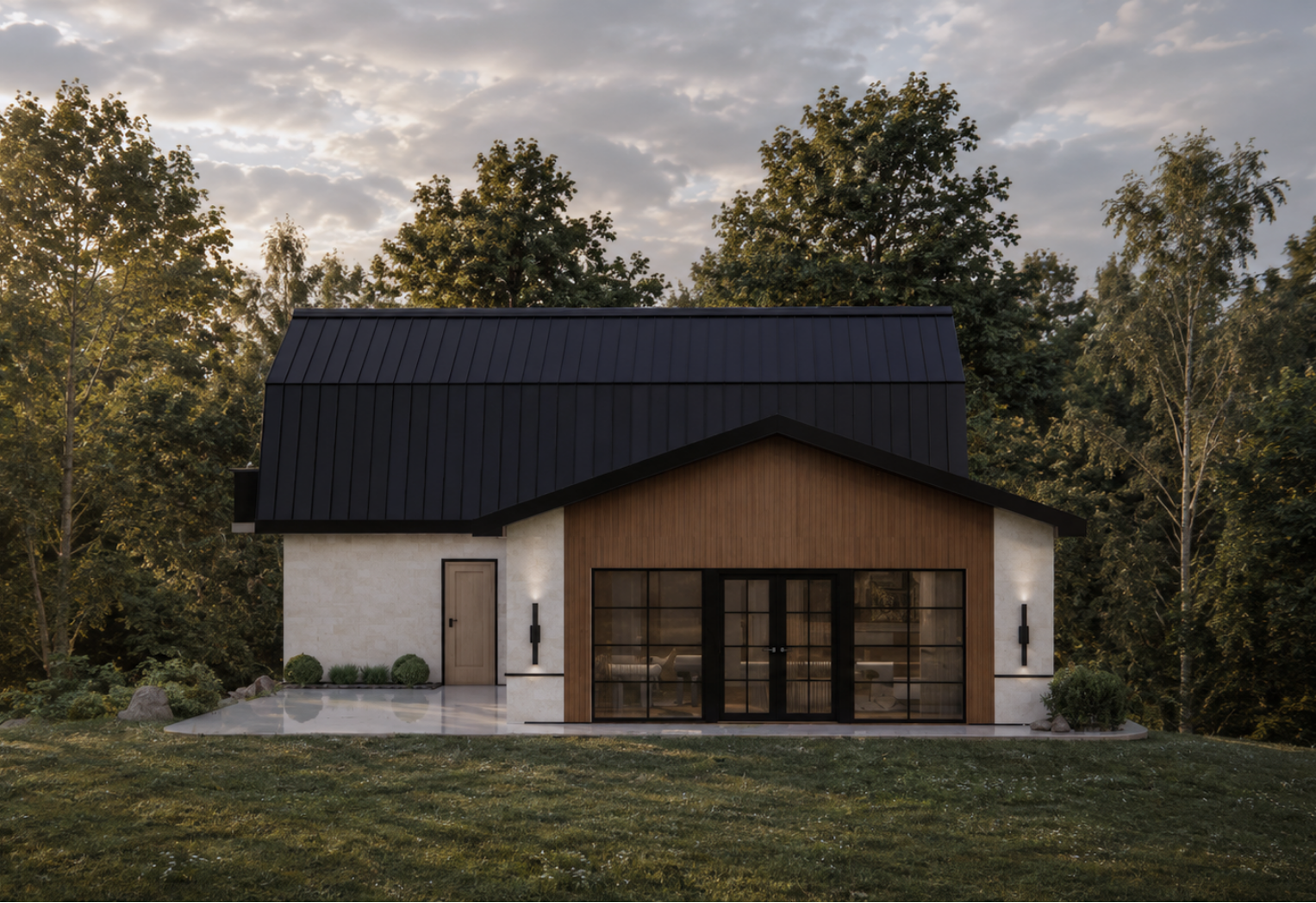 Straight-on exterior view of the modern barn-style guest house at golden hour, with vertical warm wood paneling on the central section, light stone masonry wings, a steep black metal roof, black-framed French doors and a stone patio in a forest clearing