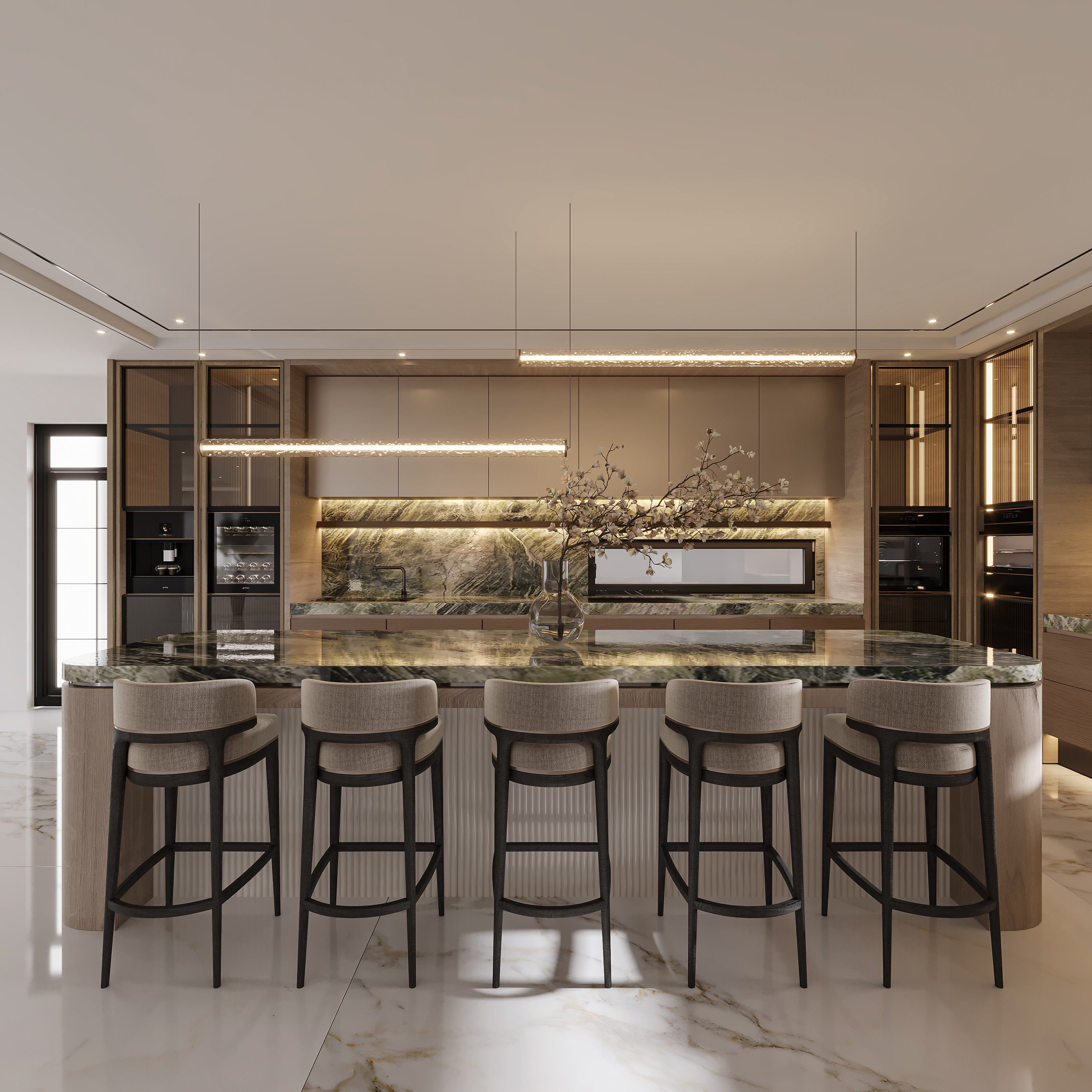 Symmetrical kitchen view across a green marble island with five upholstered bar stools, fluted travertine base, backlit green marble backsplash, blossom branches in glass and twin linear crystal pendants