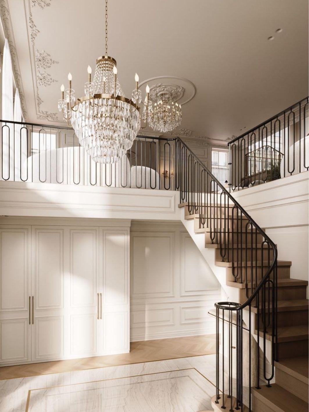 Entrance hall with full-height panelled joinery in cream with brass pulls, an oak staircase with black ironwork balustrade, crystal basket chandelier and marble floor with a brass inlay border