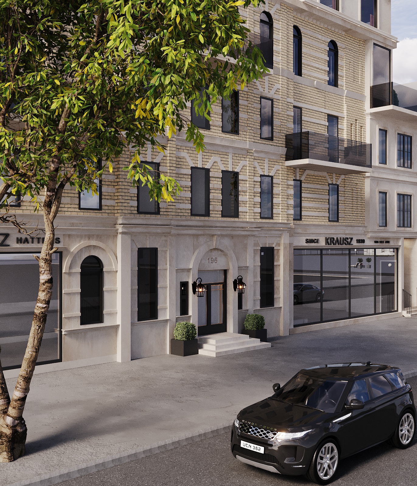 Close view of the arched cast-stone residential entry with black lantern sconces, gridded glass doors, clipped box planters and stone steps, framed by the glazed retail bays and a street tree