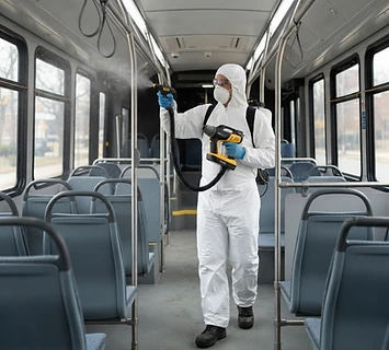 Technician in protective coveralls and gloves using professional spray equipment inside a transit vehicle