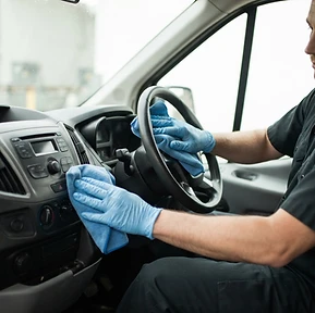 Gloved technician wiping a steering wheel and dashboard controls inside a commercial van