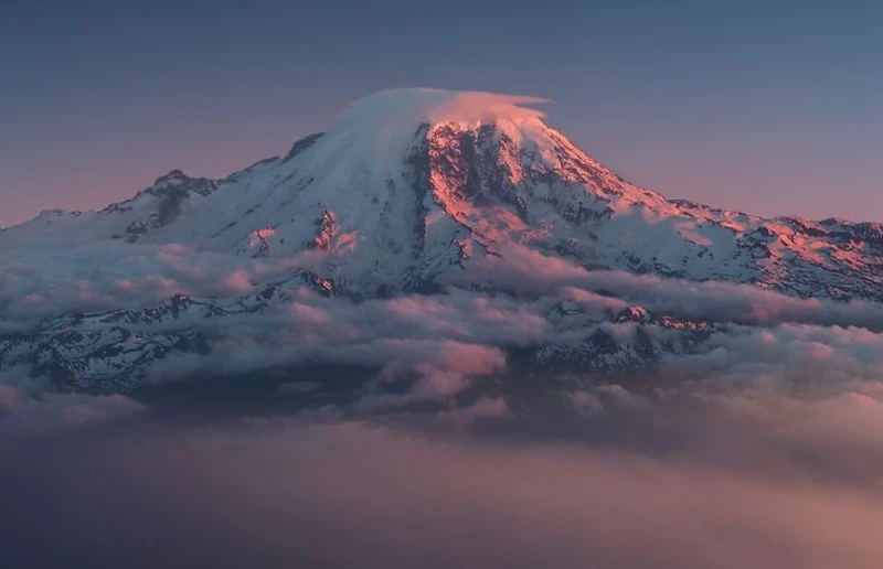 Mount Rainier's summit capped by a lenticular cloud at twilight above a sea of clouds