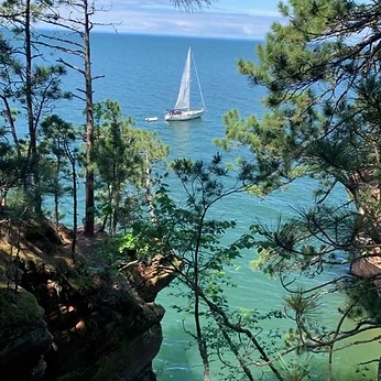 Sailboat on Lake Superior seen from a tree-lined cliff