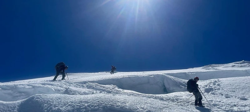 Climbers ascending a steep glaciated slope under a deep blue sky