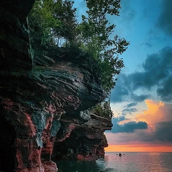 Kayaker on Lake Superior below a sandstone cliff at dusk