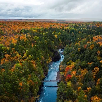 Aerial view of a river winding through fall forest past a footbridge