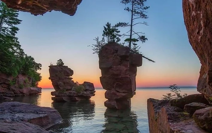 Sandstone sea stack framed by rock overhangs at sunset