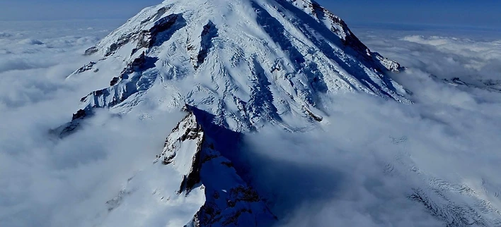 Aerial view of Mount Rainier's crevasse-scarred summit rising from a sea of clouds