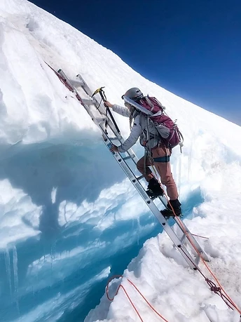 Climber stepping up an aluminum ladder across a blue crevasse