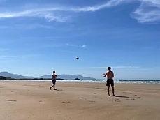 Nathan and a friend playing football shirtless on a beach