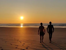 Two silhouettes walking on a wet beach at sunset