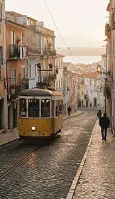 A yellow Lisbon tram on a steep cobblestone street at golden hour