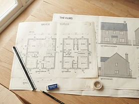 Architectural drawings of a UK house build spread across a desk