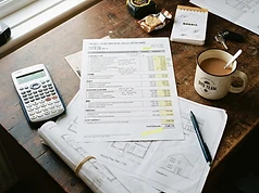 A builder's desk with a printed cost estimate, calculator and house plans