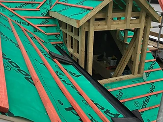 Dormer window roof under construction with green underlayment and timber battens
