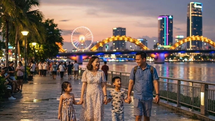 A family walking along the Han River promenade in Da Nang at dusk, with colorful bridge lights and the city skyline in the background.