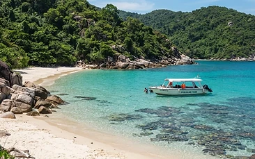 Clear turquoise water and a sandy cove on Hon Lao in the Cham Islands, with a speedboat moored near green forested hills.