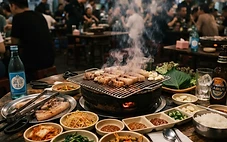 밤에 다낭의 한 식당 테이블 위에서 삼겹살이 지글지글 익어가는 고기 불판과 쌈 채소, 작은 반찬 그릇들.