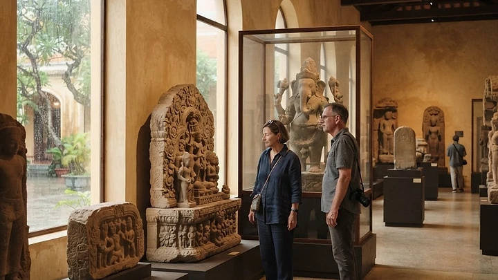 Visitors walking quietly among ancient sandstone Cham sculptures in a bright, airy museum gallery in Da Nang on a rainy afternoon.