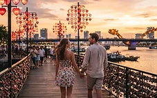 A couple walking along the Love Bridge in Da Nang at sunset with heart-shaped lanterns glowing.