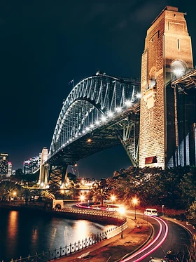 Sydney Harbour Bridge glowing at night with red light trails along the harbour road