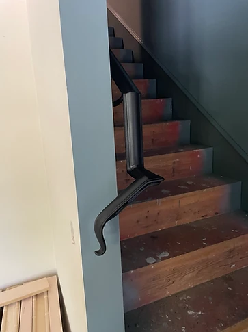 Lower return of the forged handrail with scrolled lamb's-tongue end beside painted millwork