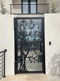 Pedestrian gate with decorative metal tree silhouette and textured privacy glass