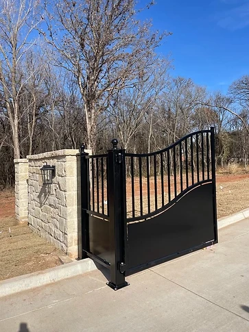 Close view of the modern driveway gate's curved panel line and vertical picket section beside a stone column