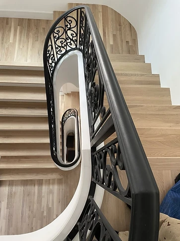 Close view of the shaped handrail and ornamental scrollwork detail on the curved stair railing