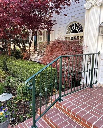 Detail of the green exterior entry railing with scrolled end volute and collar detailing over brick steps