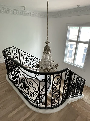 Ornamental iron railing wrapping the curved stair landing beneath a chandelier