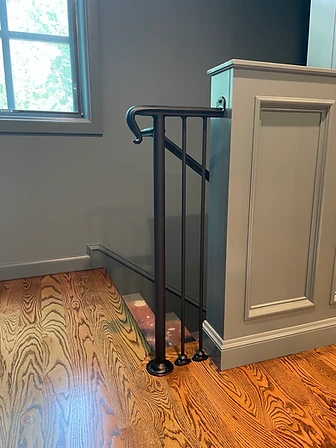 Forged black interior stair handrail with scrolled return and vertical pickets at a finished landing