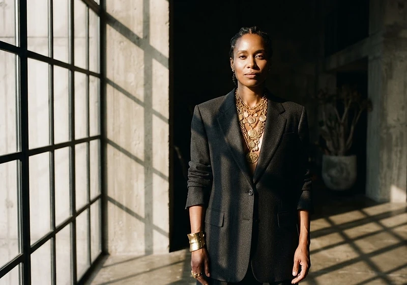 A woman wearing layered gold regalia in a brutalist architectural interior
