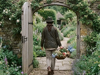 A gardener walking through a gate into an established English garden
