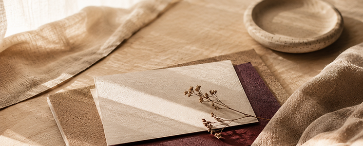 Composition éditoriale de papiers texturés, touche prune et lumière naturelle sur matière bois et lin.