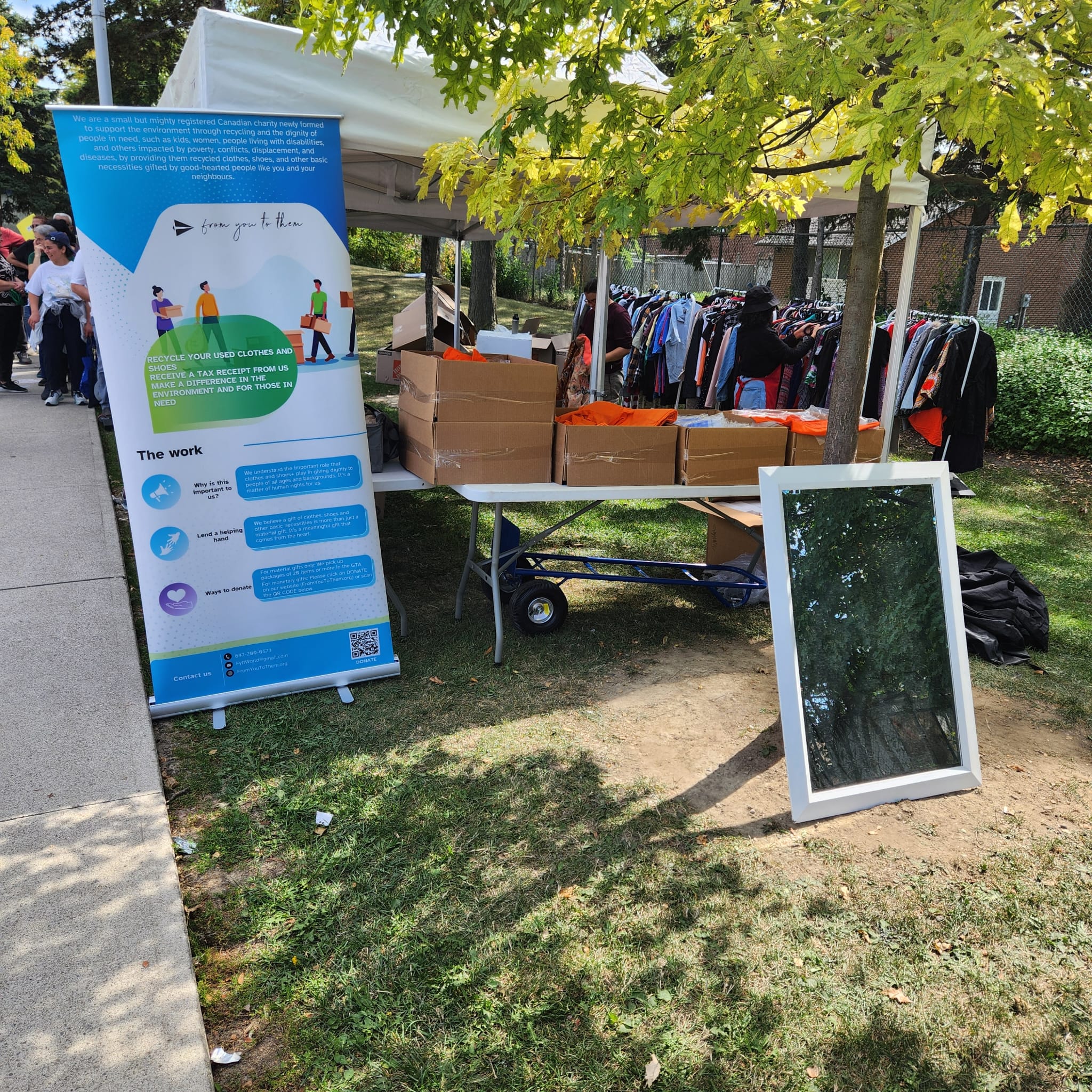 Outdoor clothing drive with garment racks, a standing mirror and donation boxes under a white tent