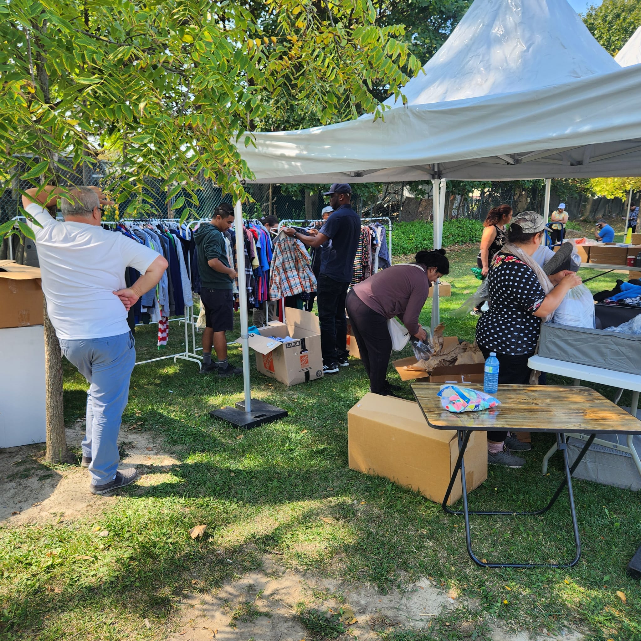 Volunteers sorting clothing under a white canopy tent at an outdoor community drive