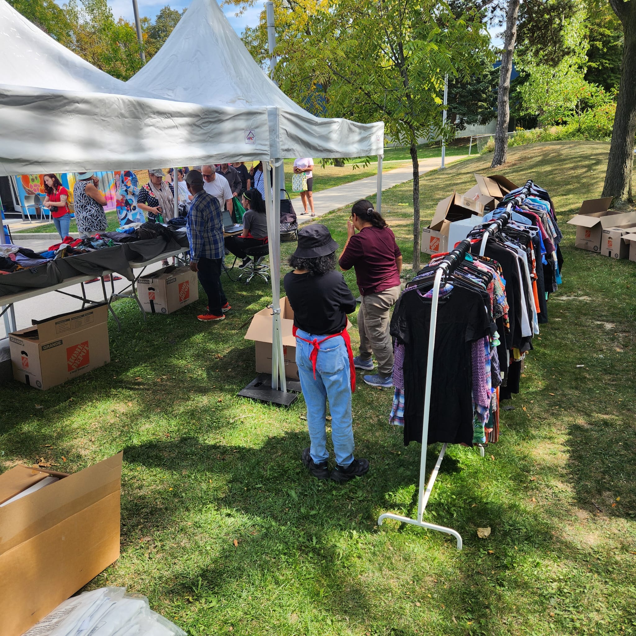 A volunteer in a red apron sorting through garments on a clothing rack at an outdoor event