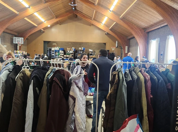 A community member selecting coats from garment racks at a From You To Them clothing distribution
