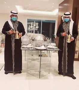 قهوجيان بزي أبيض يحملان دلال ذهبية ويقدمان خدمة ضيافة فاخرة