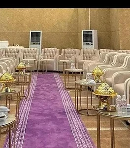 قاعة مناسبات مجهزة بكنبات بيج وبساط بنفسجي وأطقم ضيافة ذهبية فاخرة